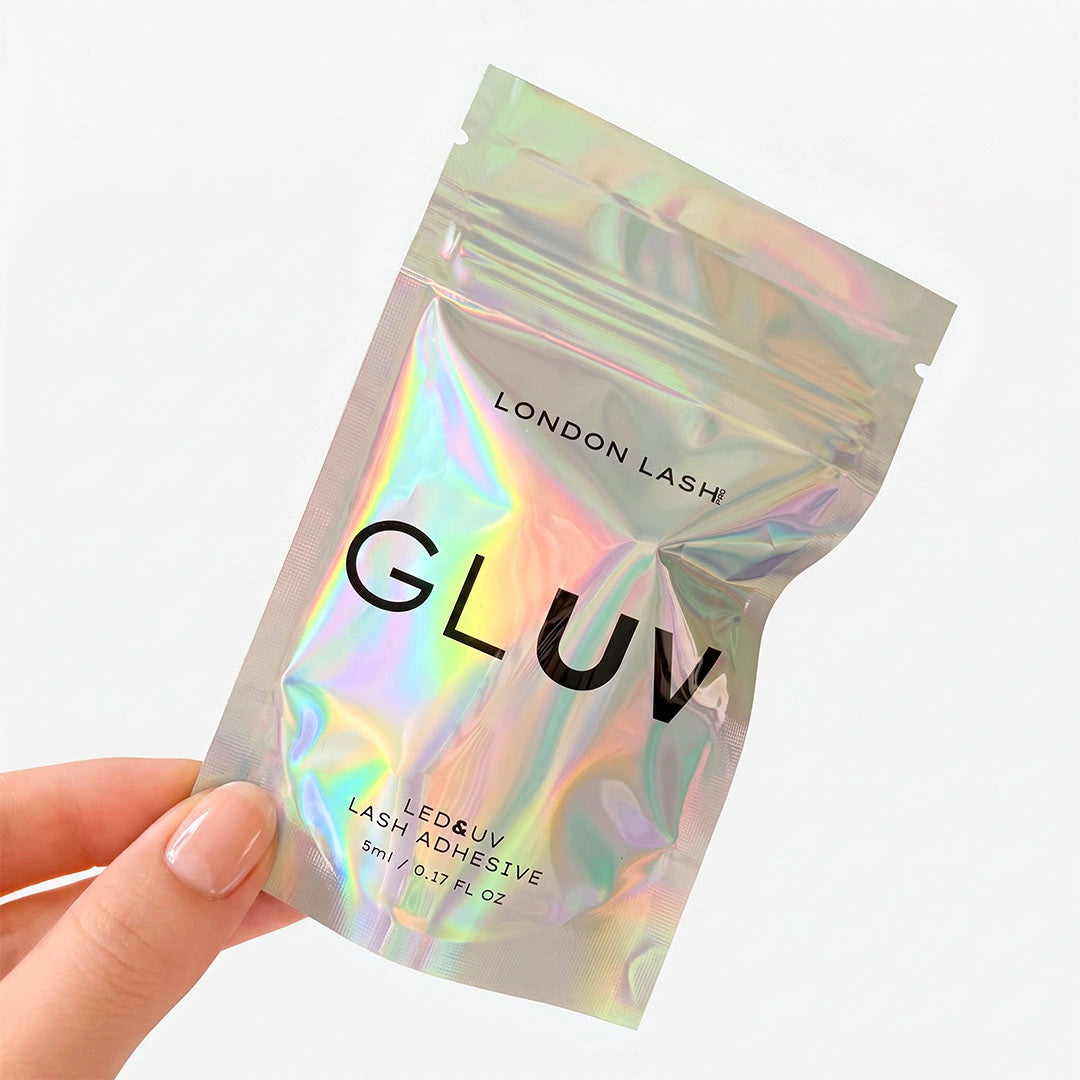 Frasco de 5 ml del adhesivo para extensiones de pestañas London Lash GLUV LED & UV con tapón metálico morado, acompañado de gotas de adhesivo transparente sobre un fondo blanco.
