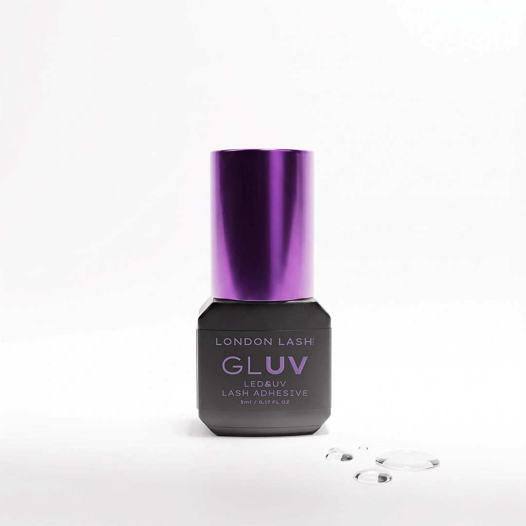 Frasco de 5 ml del adhesivo para extensiones de pestañas London Lash GLUV LED & UV con tapón metálico morado, acompañado de gotas de adhesivo transparente sobre un fondo blanco.