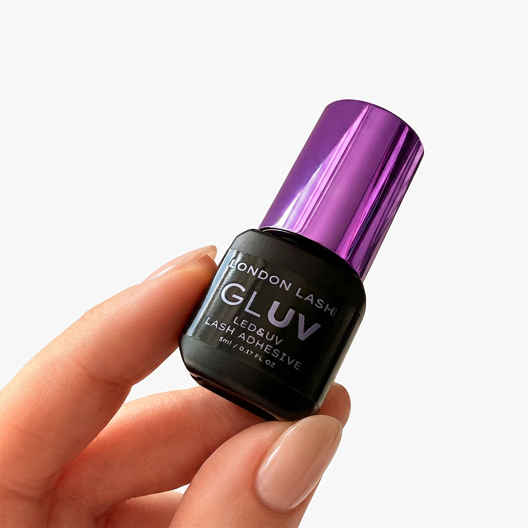Primer plano de una mano con manicura sosteniendo el frasco de 5 ml del adhesivo London Lash GLUV con un brillante tapón morado.