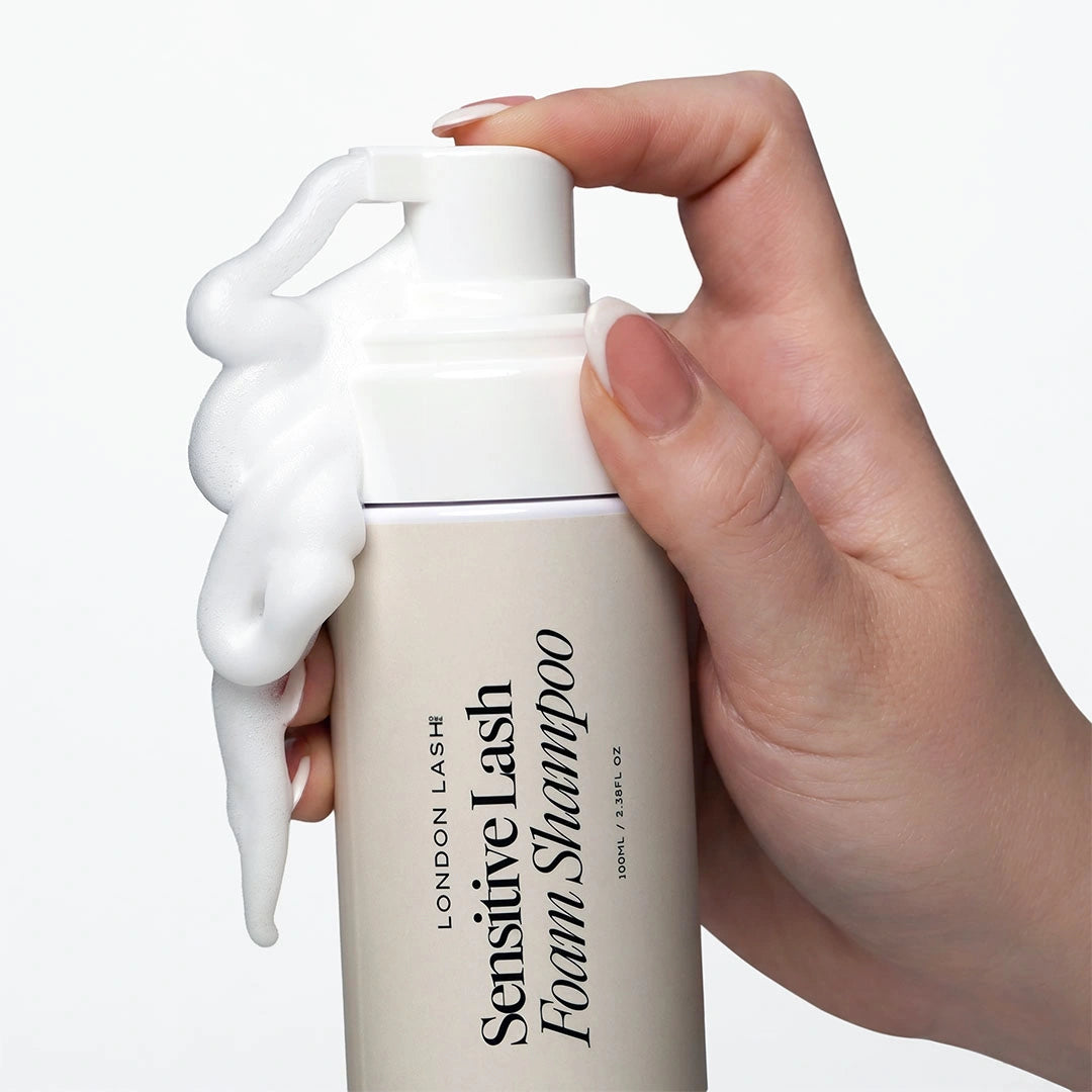 Primer plano de una mano presionando el dosificador del Sensitive Lash Foam Shampoo de London Lash mientras dispensa una espuma limpiadora abundante.