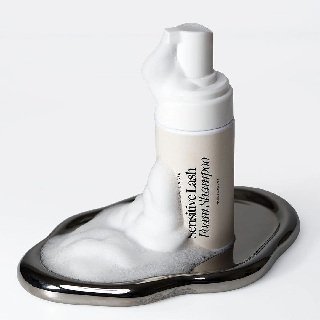 Sensitive Lash Foam Shampoo de London Lash sobre una bandeja plateada reflectante, rodeado de una abundante espuma limpiadora.