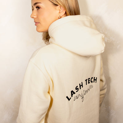 Lashista enseñando la parte de atrás de la sudadera beige con capucha de London Lash